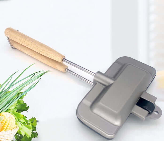 Double-sided sandwich toaster with wooden handle on kitchen counter, fresh vegetables nearby