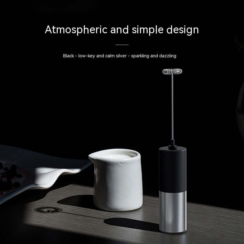 Electric milk frother and white ceramic creamer on a wooden kitchen tabletop