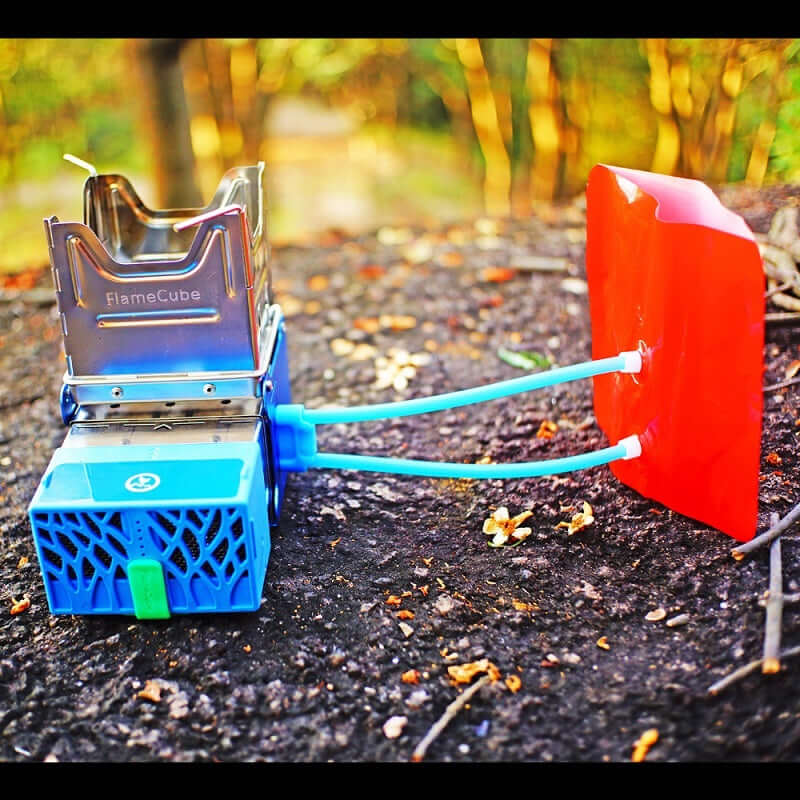 Portable stainless steel camping stove with blue and red components outdoors on forest ground