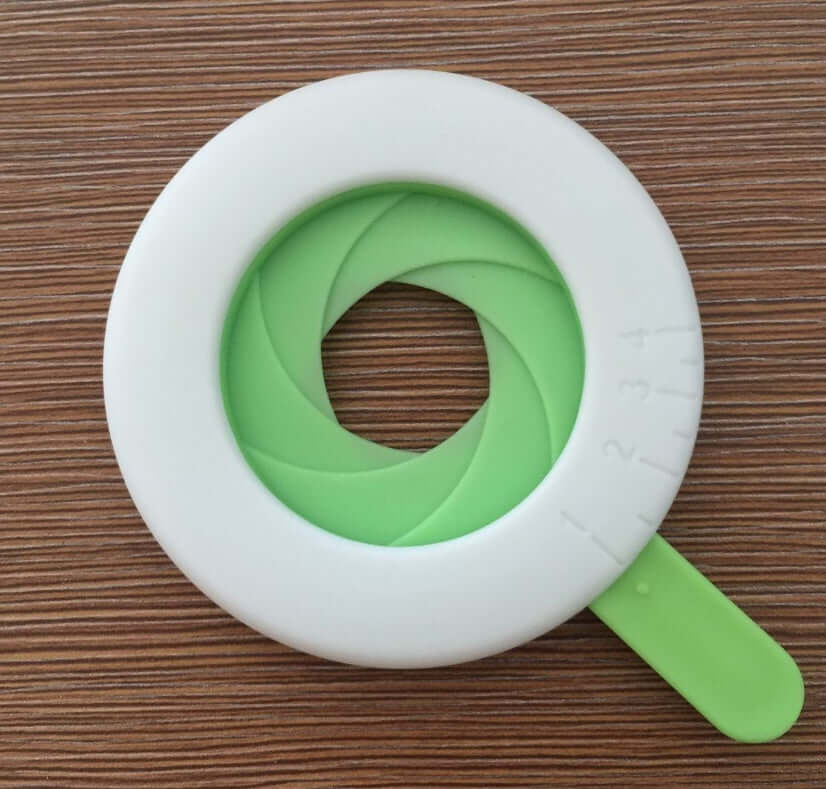 Adjustable round egg mold or kitchen ring tool with green and white design on wood background