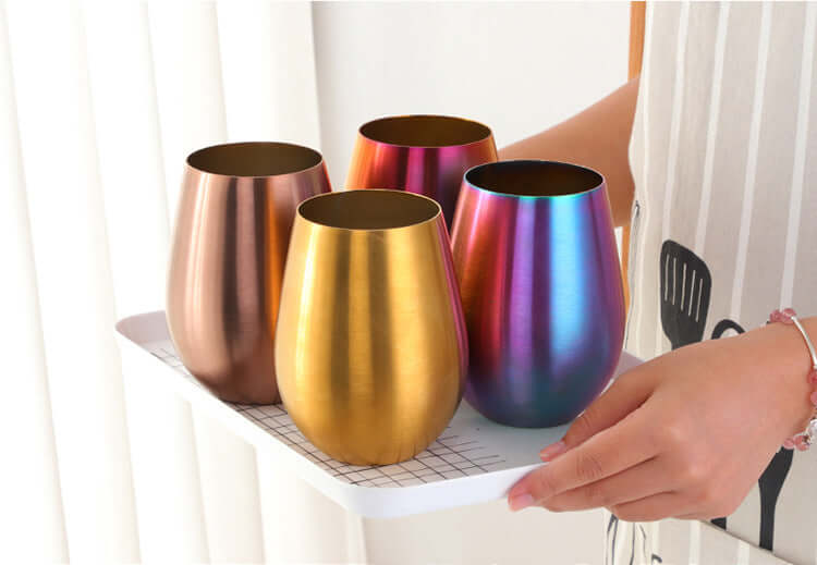 Set of metallic stainless steel tumblers in gold, bronze, and rainbow colors on a tray