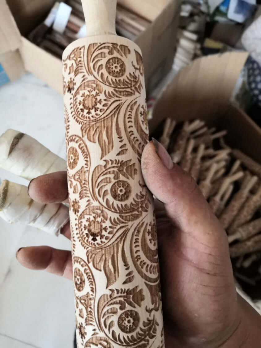 Hand holding engraved wooden rolling pin with ornate floral pattern for baking