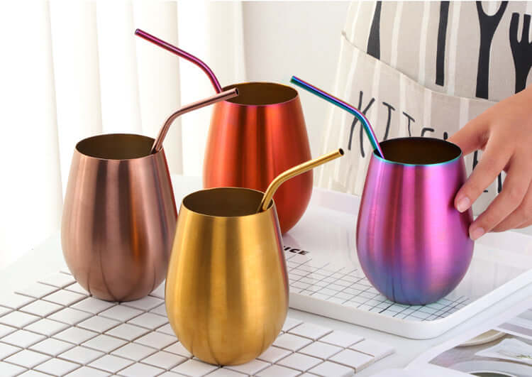 Set of four metallic stainless steel tumblers with straws in gold, red, bronze, and iridescent colors on a white tray.