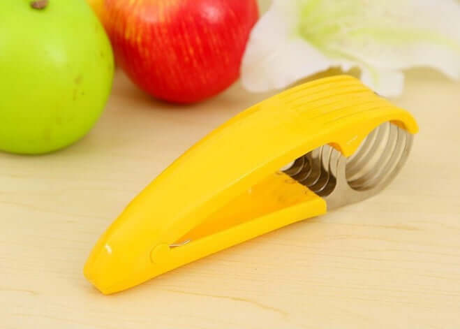 Yellow apple slicer with stainless steel blades on kitchen counter, apples in background