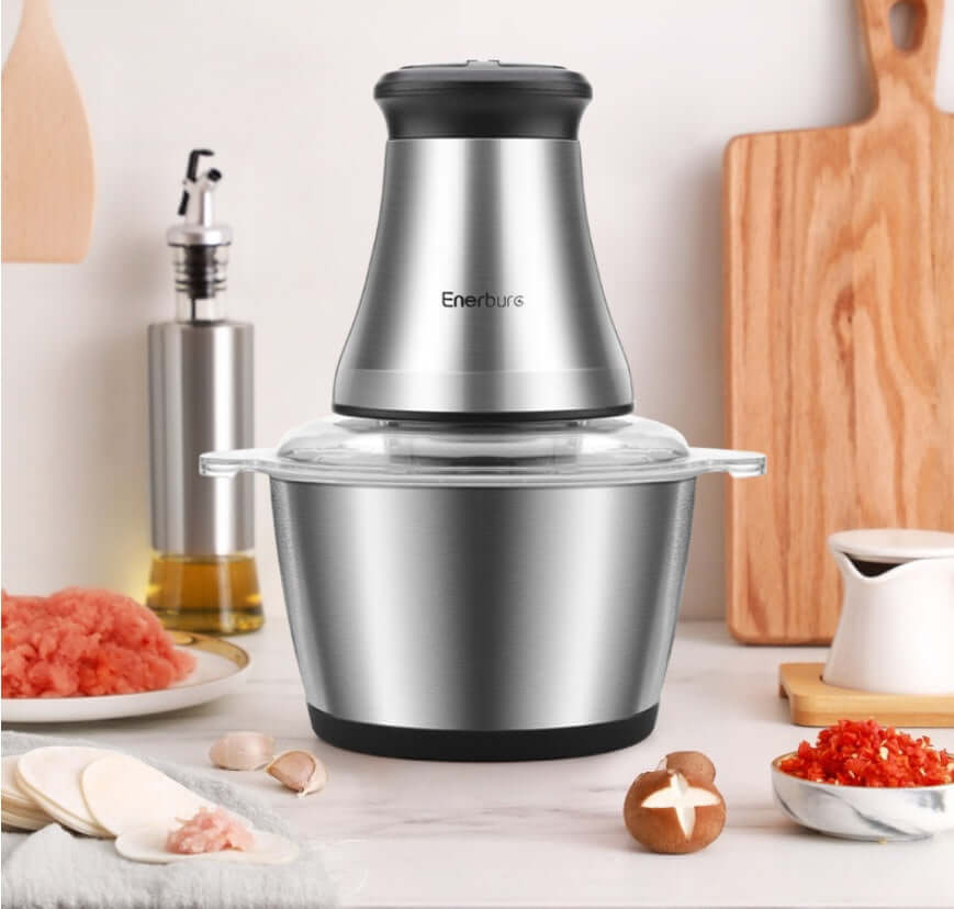 Stainless steel electric food chopper on kitchen counter with fresh ingredients and utensils.