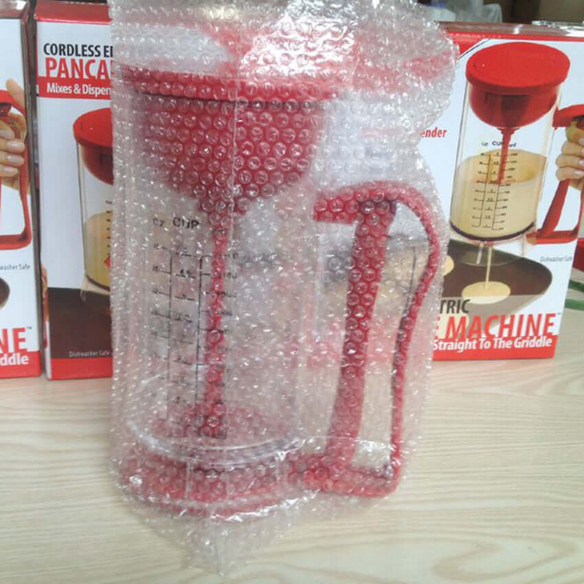 Red pancake batter dispenser wrapped in bubble wrap on kitchen counter