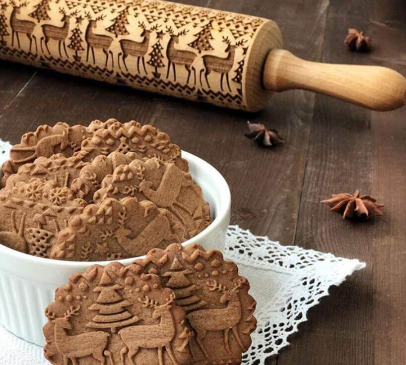 Embossed rolling pin and festive cookies with reindeer and tree patterns on wooden table