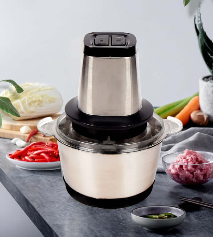 Stainless steel electric food chopper on kitchen counter with vegetables and meat