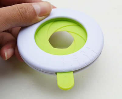 Hand holding a round green and white kitchen tool for opening jars or bottles