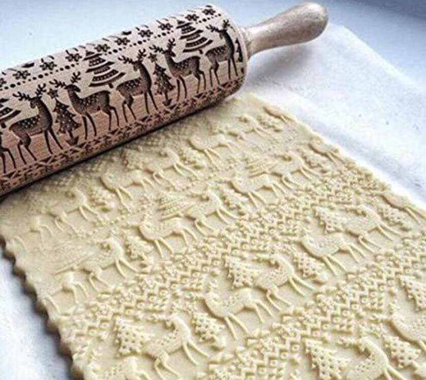 Engraved rolling pin with deer and tree pattern imprinting festive cookie dough