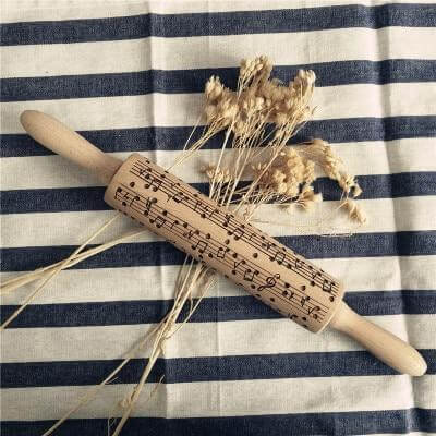 Wooden rolling pin with music notes pattern, placed on striped cloth with dried flowers, kitchen accessory.