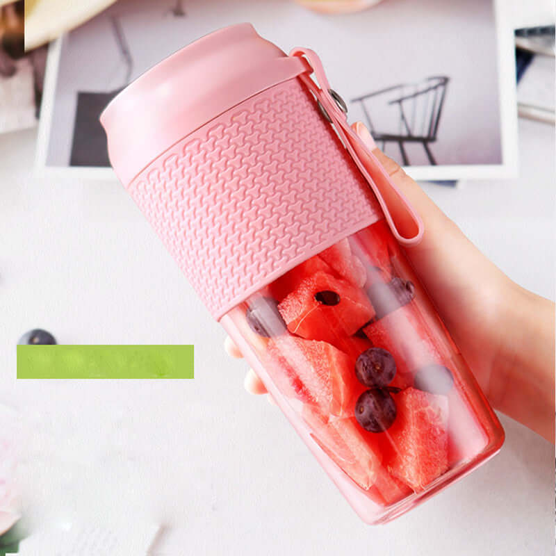 Portable pink blender cup filled with watermelon and grapes, held by hand on kitchen table