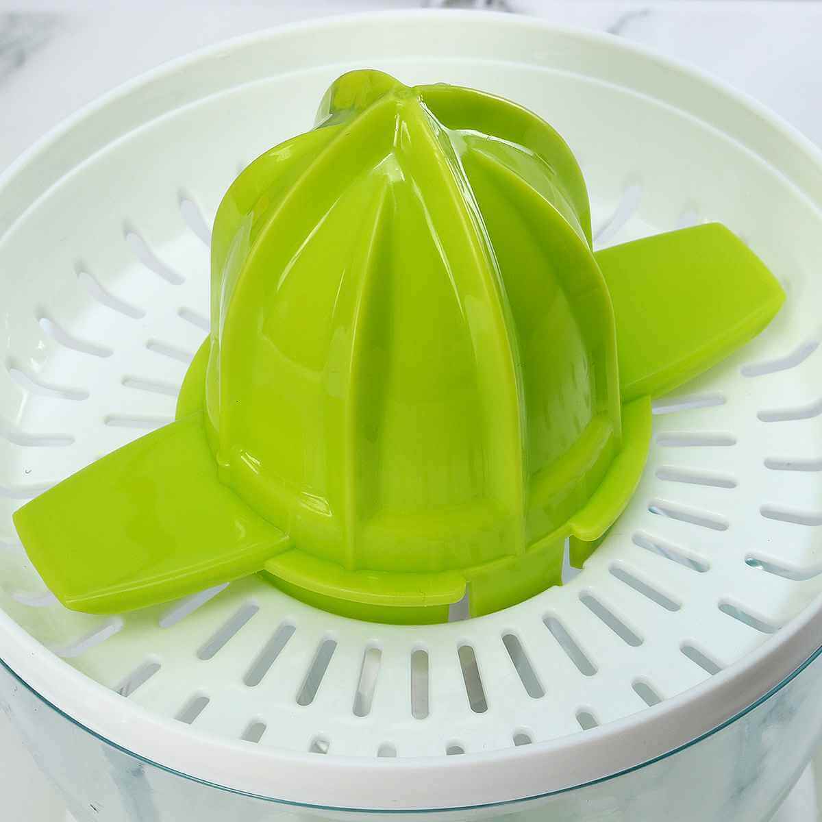 Green manual citrus juicer with strainer basket on a white kitchen countertop