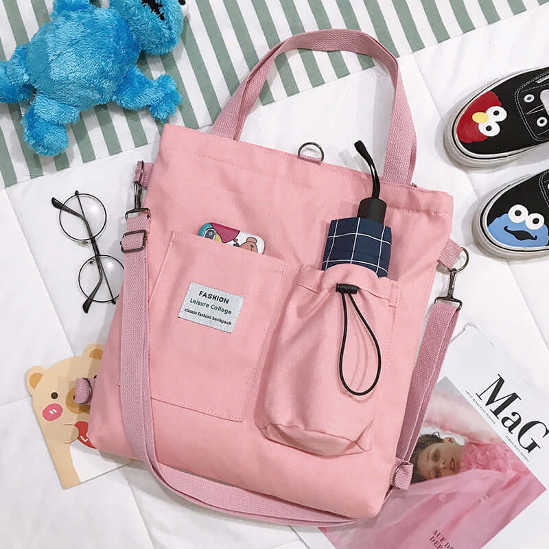 Pink canvas tote bag with front pockets, umbrella, and casual college accessories on bed