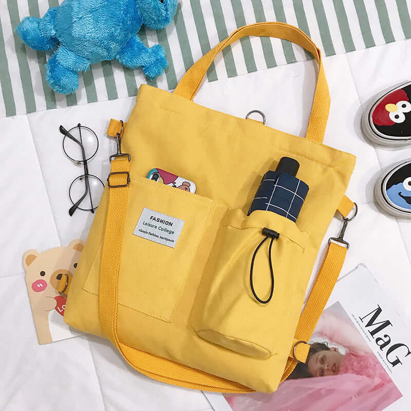 Yellow canvas tote bag with front pockets, glasses, and accessories on a bed.
