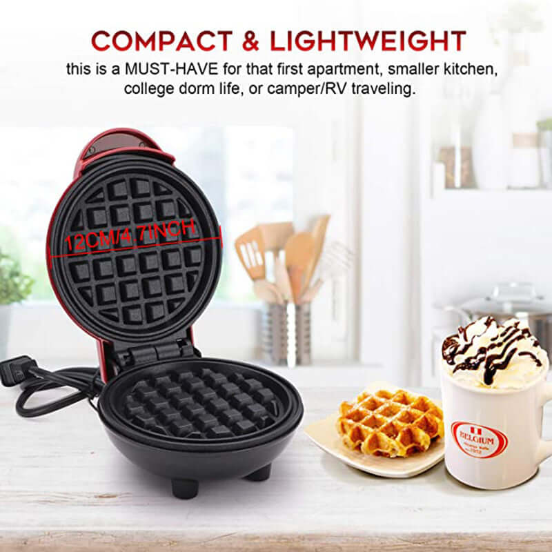 Compact round electric waffle maker with black nonstick plates on a kitchen counter, next to a plate of waffles and a mug of hot chocolate.