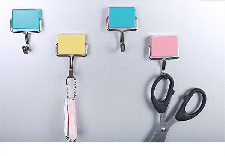 Colorful adhesive wall hooks holding kitchen scissors and utensils on a grey surface