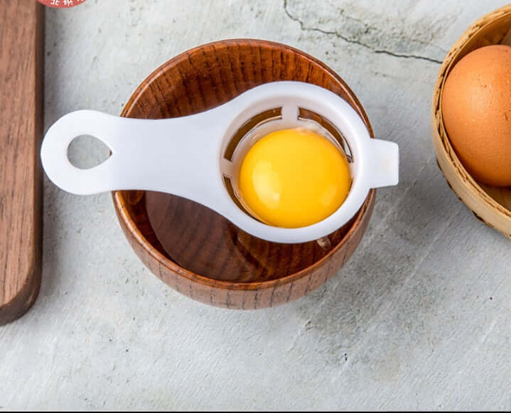 Egg separator kitchen tool with egg yolk over wooden bowl, egg in basket nearby
