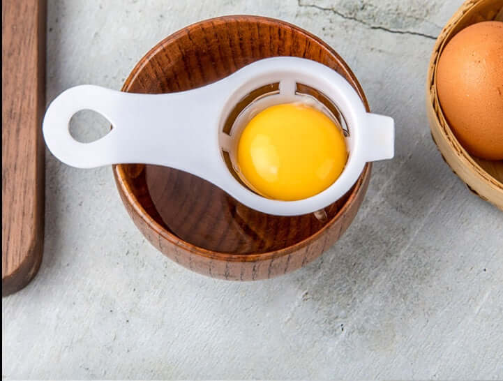 Egg yolk separator kitchen tool over wooden bowl with an egg yolk inside, on countertop