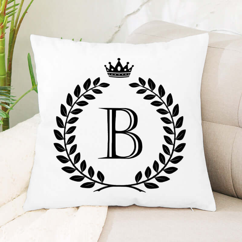 White throw pillow with black letter B, laurel wreath, and crown design on couch
