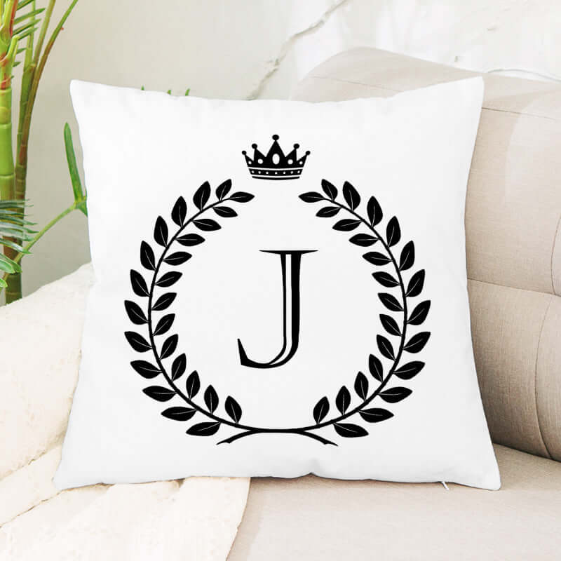 Monogram throw pillow with letter J, laurel wreath, and crown on a white couch