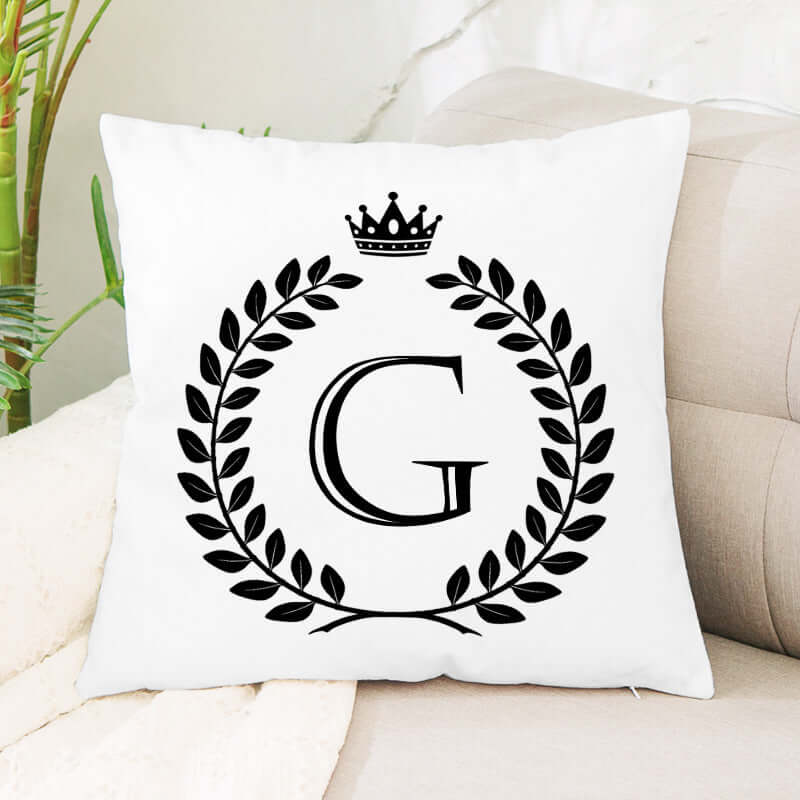 White throw pillow with black letter G, laurel wreath, and crown design on sofa