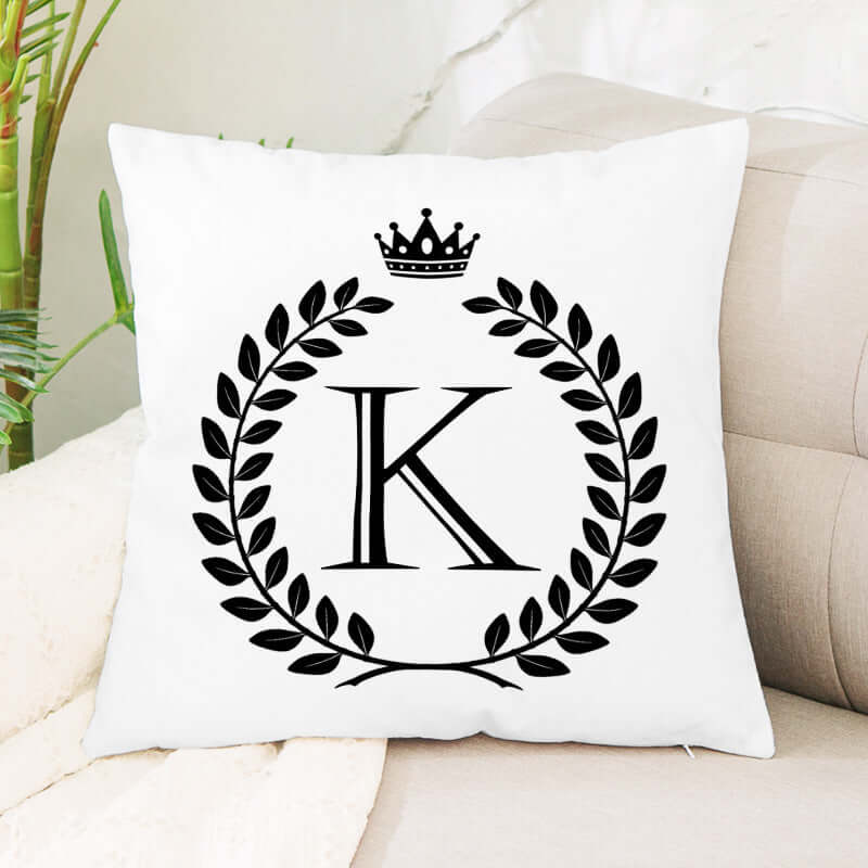 White decorative pillow with letter K, laurel wreath, and crown design on a beige sofa