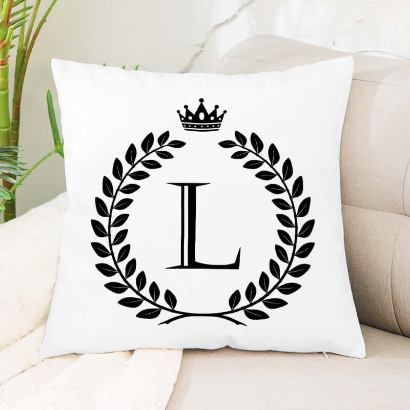 White throw pillow with black letter L, laurel wreath, and crown design on sofa