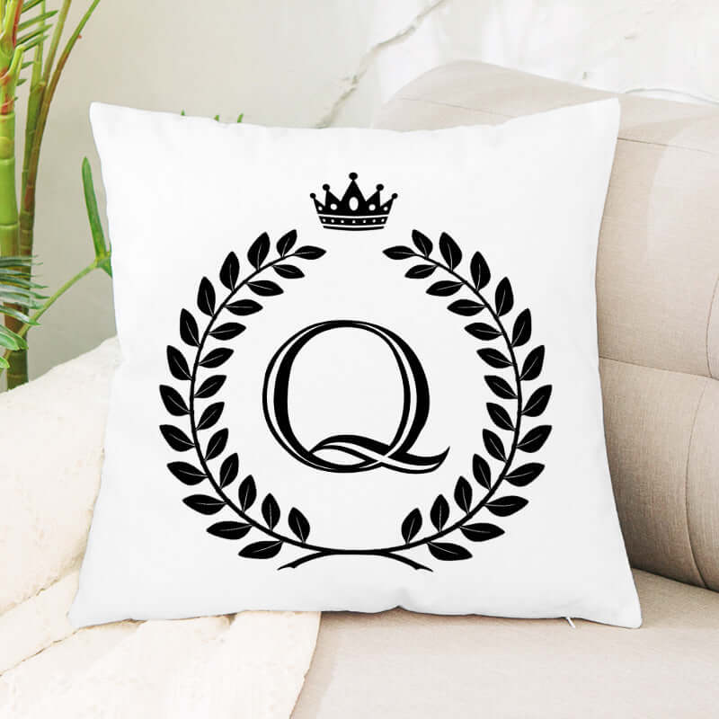 White decorative throw pillow with black letter Q, crown, and laurel wreath design on a couch