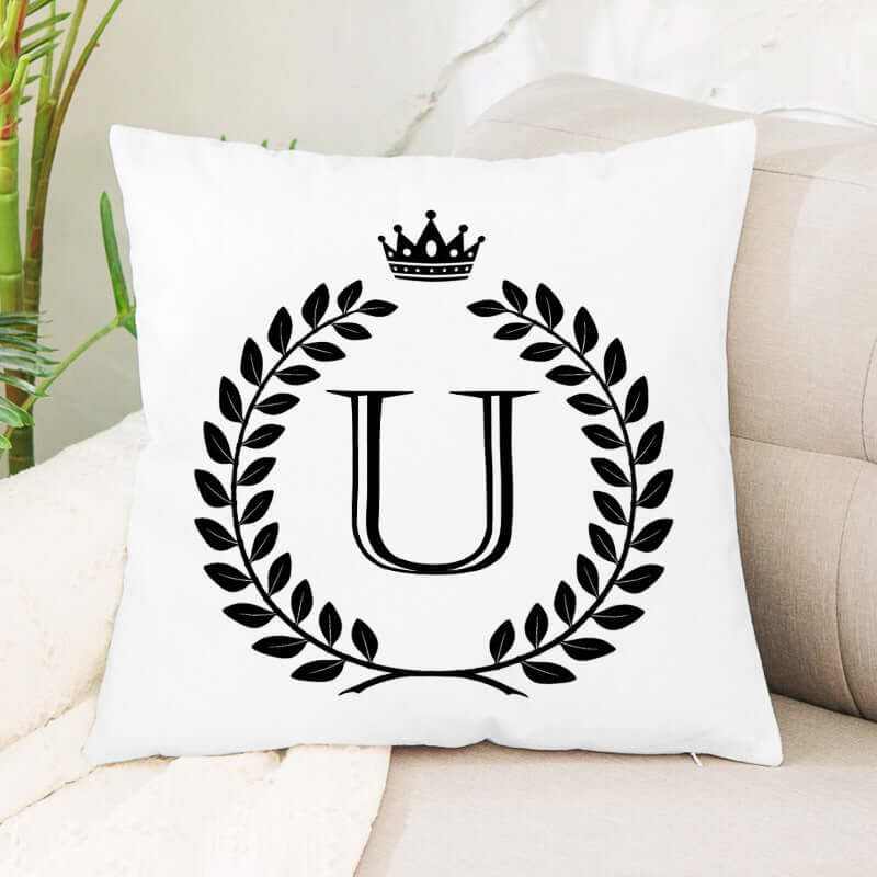 White decorative throw pillow with black letter U, laurel wreath, and crown design on sofa