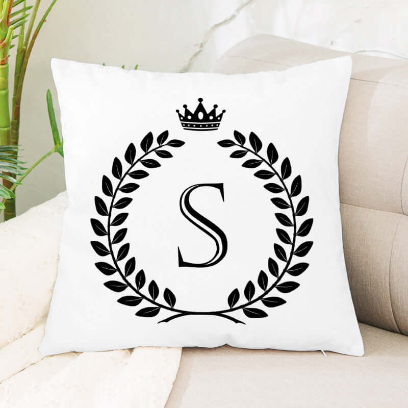 White decorative throw pillow with black monogram letter S, laurel wreath, and crown design