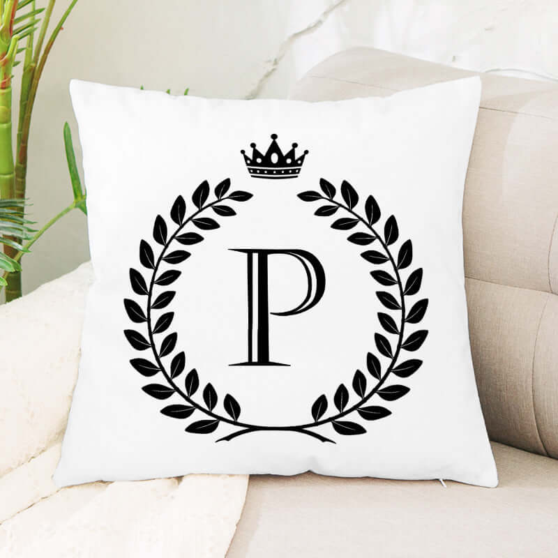 White decorative throw pillow with black laurel wreath, crown, and letter P design on sofa