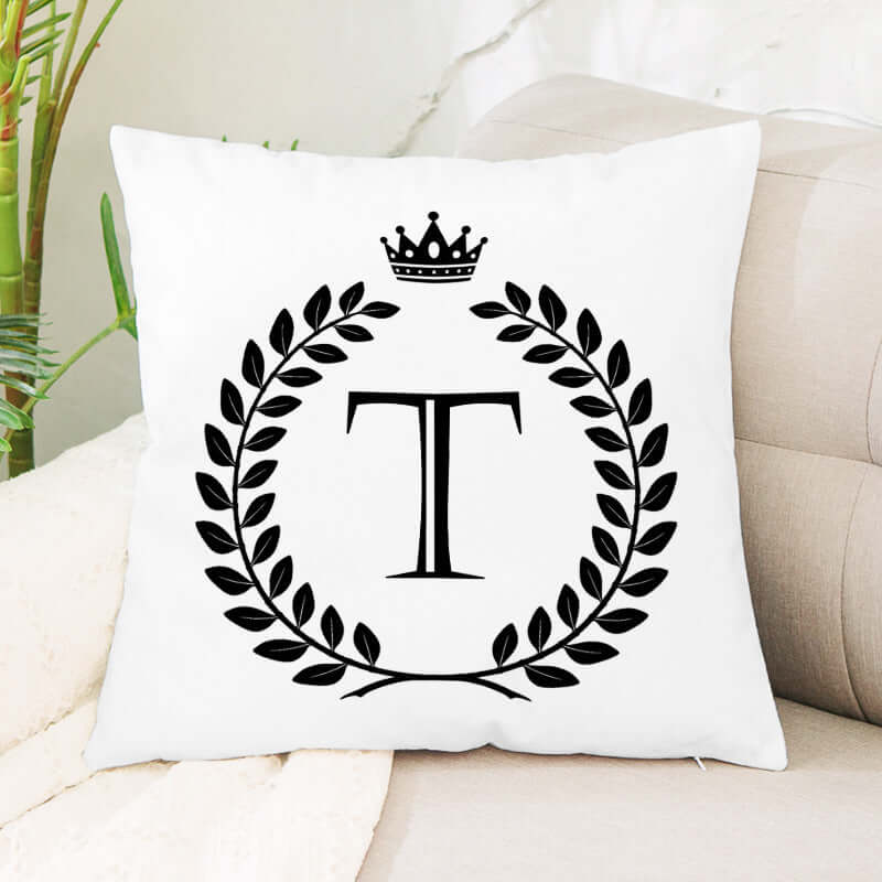 White decorative pillow with black initial T, laurel wreath, and crown design on a couch