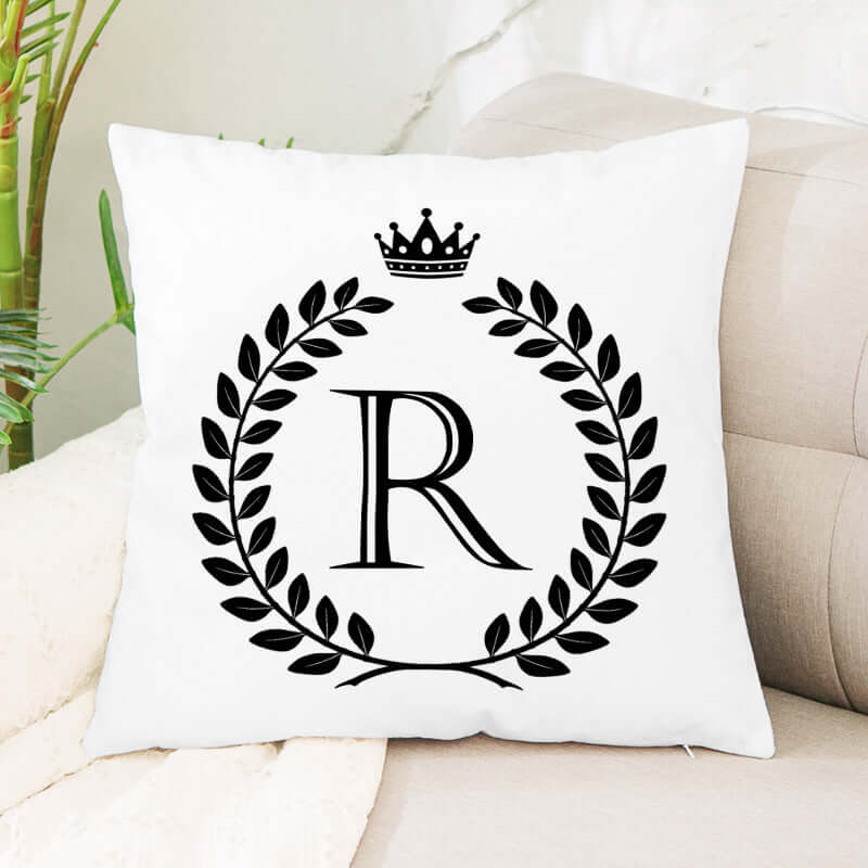 White decorative throw pillow with black letter R, laurel wreath, and crown design on sofa