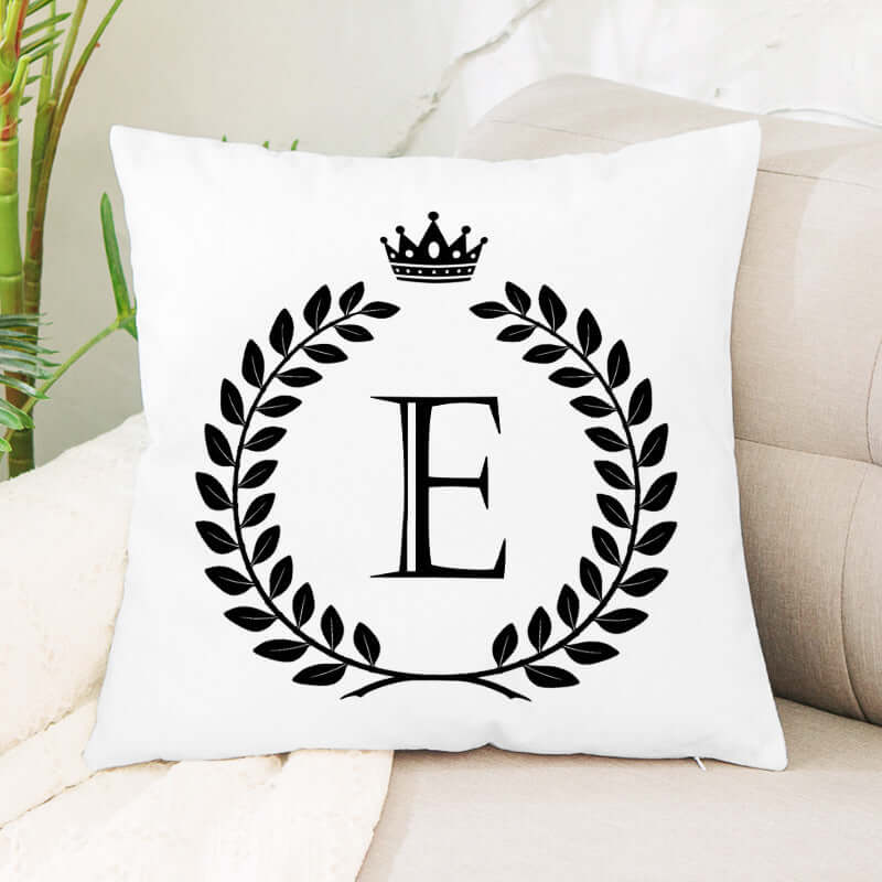 White decorative throw pillow with black letter E, laurel wreath, and crown design on sofa