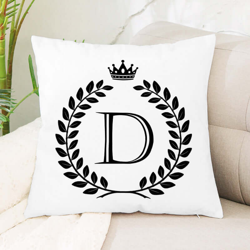 White decorative throw pillow with black letter D, laurel wreath, and crown design on a sofa