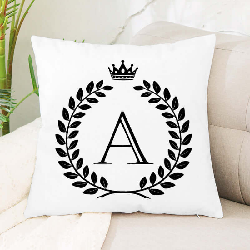 White throw pillow with letter A, laurel wreath and crown design on couch
