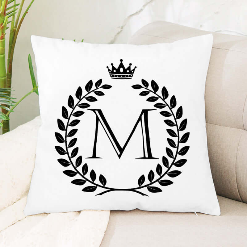 White decorative pillow with black monogram M, laurel wreath, and crown design on sofa
