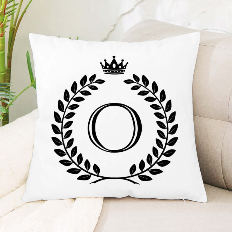 White decorative pillow with black letter O, laurel wreath, and crown design on a sofa