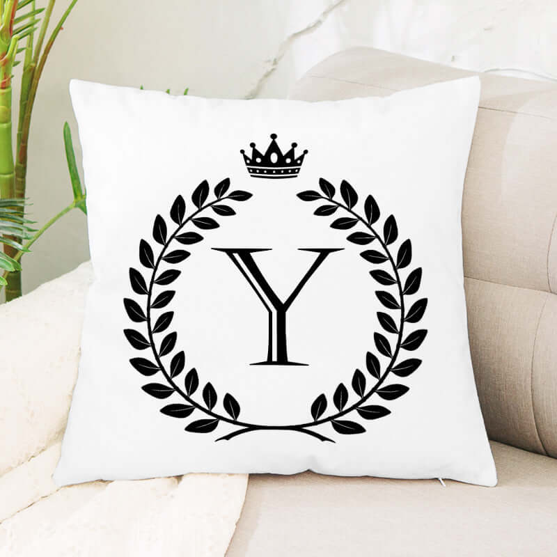White decorative throw pillow with black letter Y, laurel wreath, and crown design on sofa