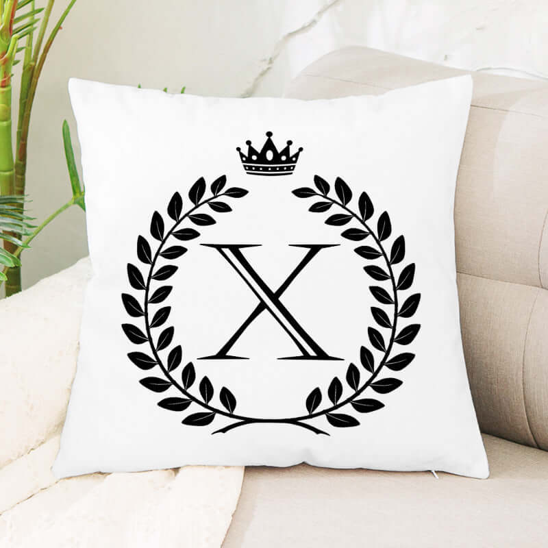 White decorative pillow with black laurel wreath, crown, and large letter X design