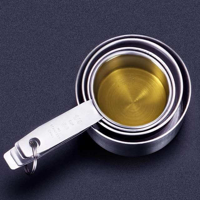 Stacked stainless steel measuring cups with liquid on a dark kitchen countertop