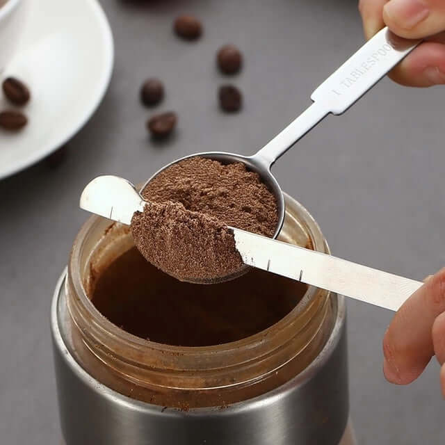 Stainless steel coffee measuring spoon with leveler scooping ground coffee from a jar
