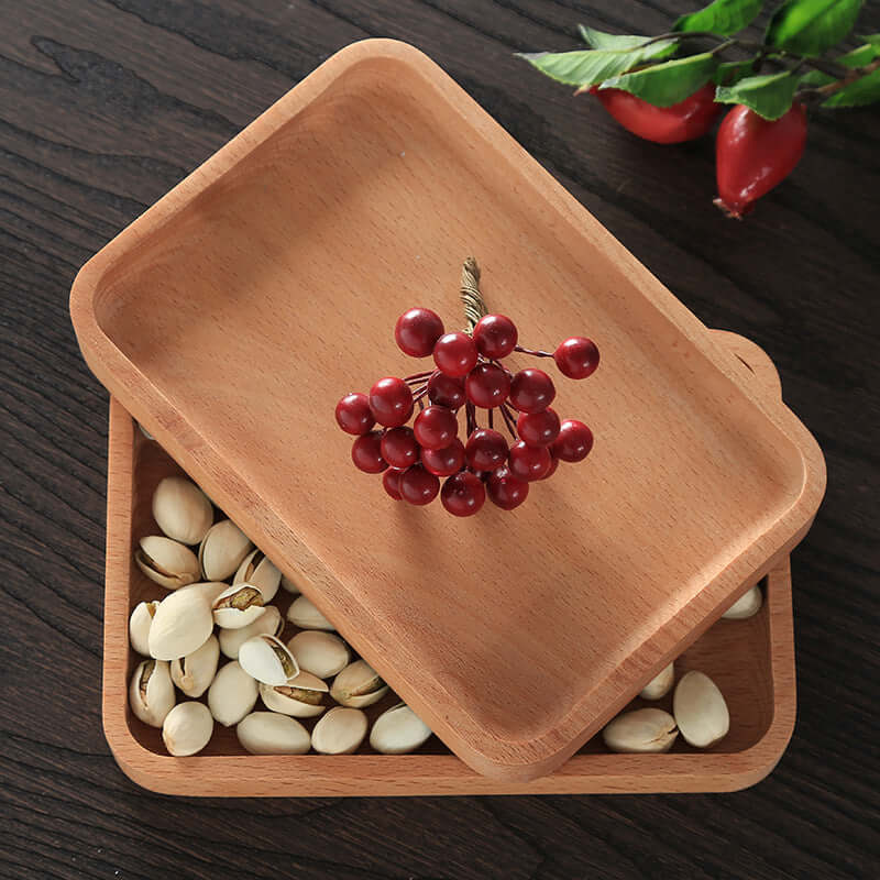 Wooden serving trays with pistachios and red artificial berries on dark wood table