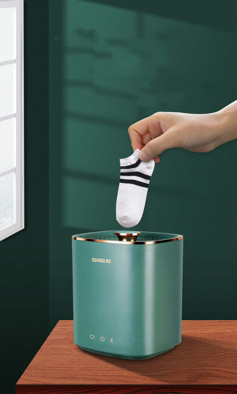 Hand placing a small white sock into a green compact washing machine on a wooden surface