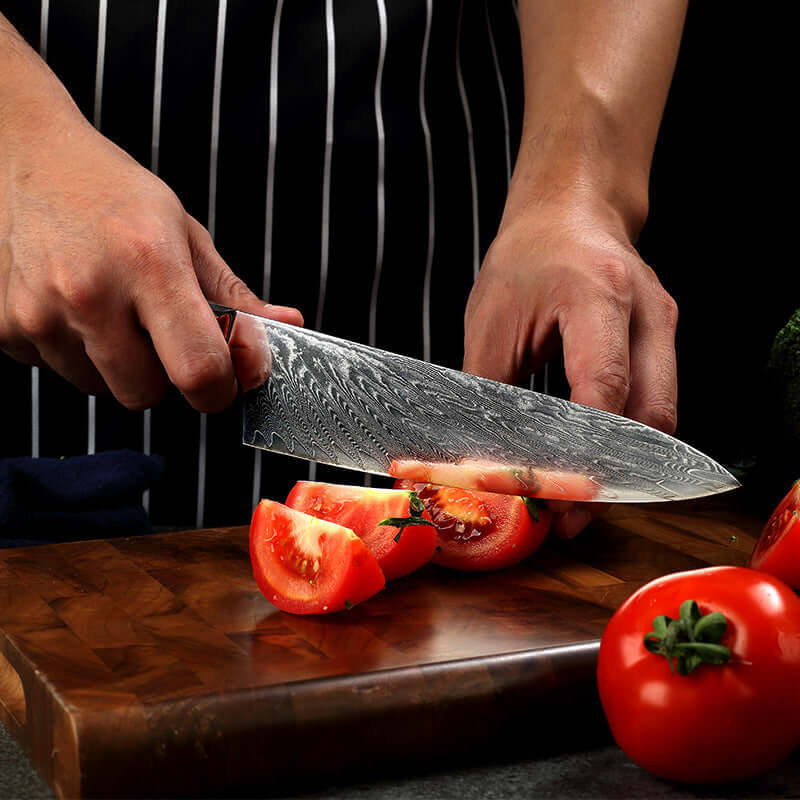 Chef slicing tomato with Damascus steel kitchen knife on wooden cutting board