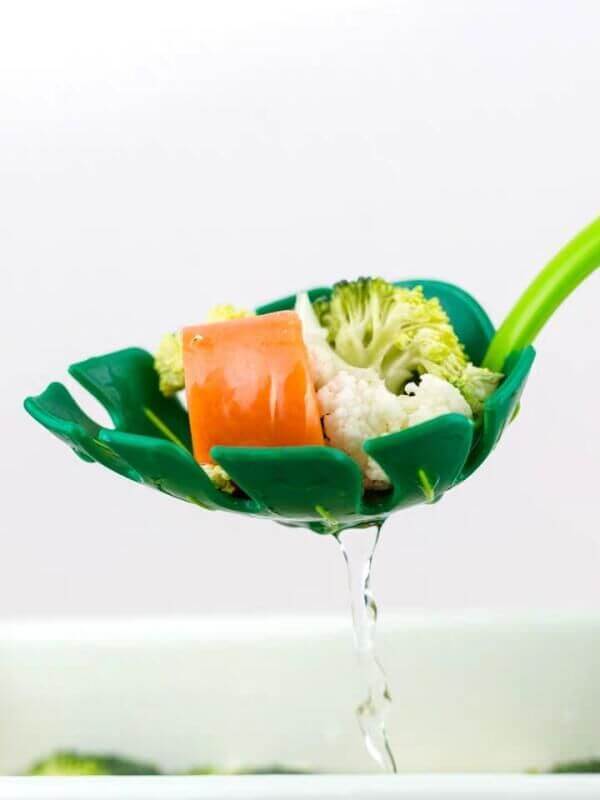Green kitchen strainer spoon draining steamed vegetables including broccoli, cauliflower, and carrot