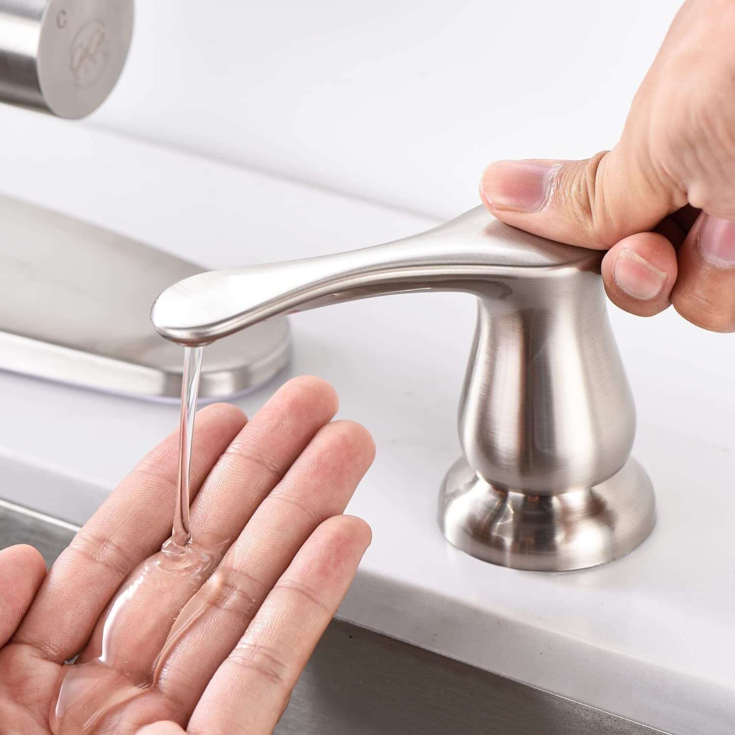 Brushed stainless steel kitchen soap dispenser dispensing liquid onto a hand at sink