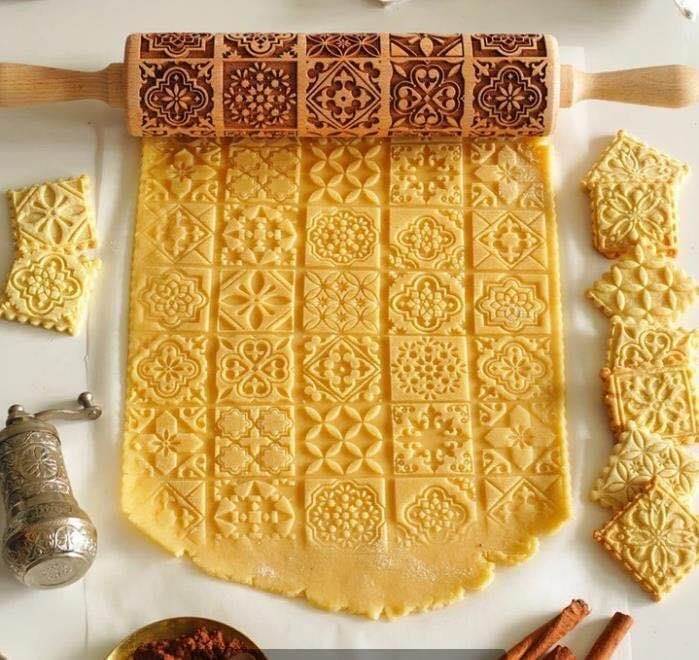 Embossed wooden rolling pin creating decorative patterns on cookie dough, kitchen accessory.