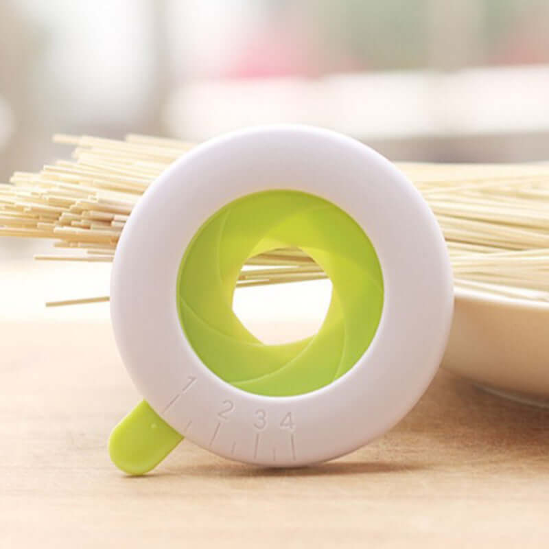 Adjustable spaghetti pasta measuring tool with white and green circular design on a kitchen table